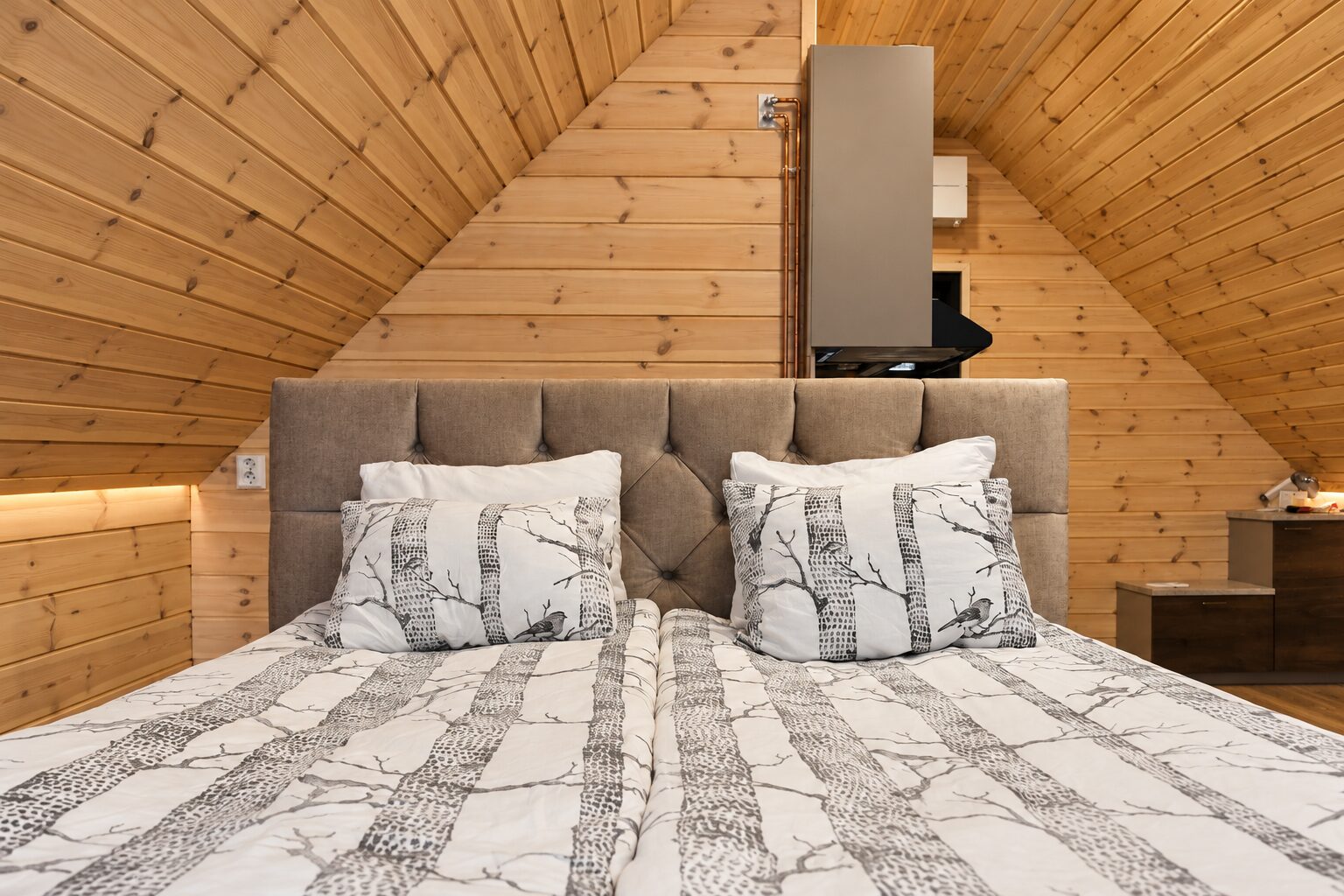 Doppelbett mit gepolstertem Kopfteil und Bettwäsche mit Birkenmuster in einem holzvertäfelten Schlafbereich
