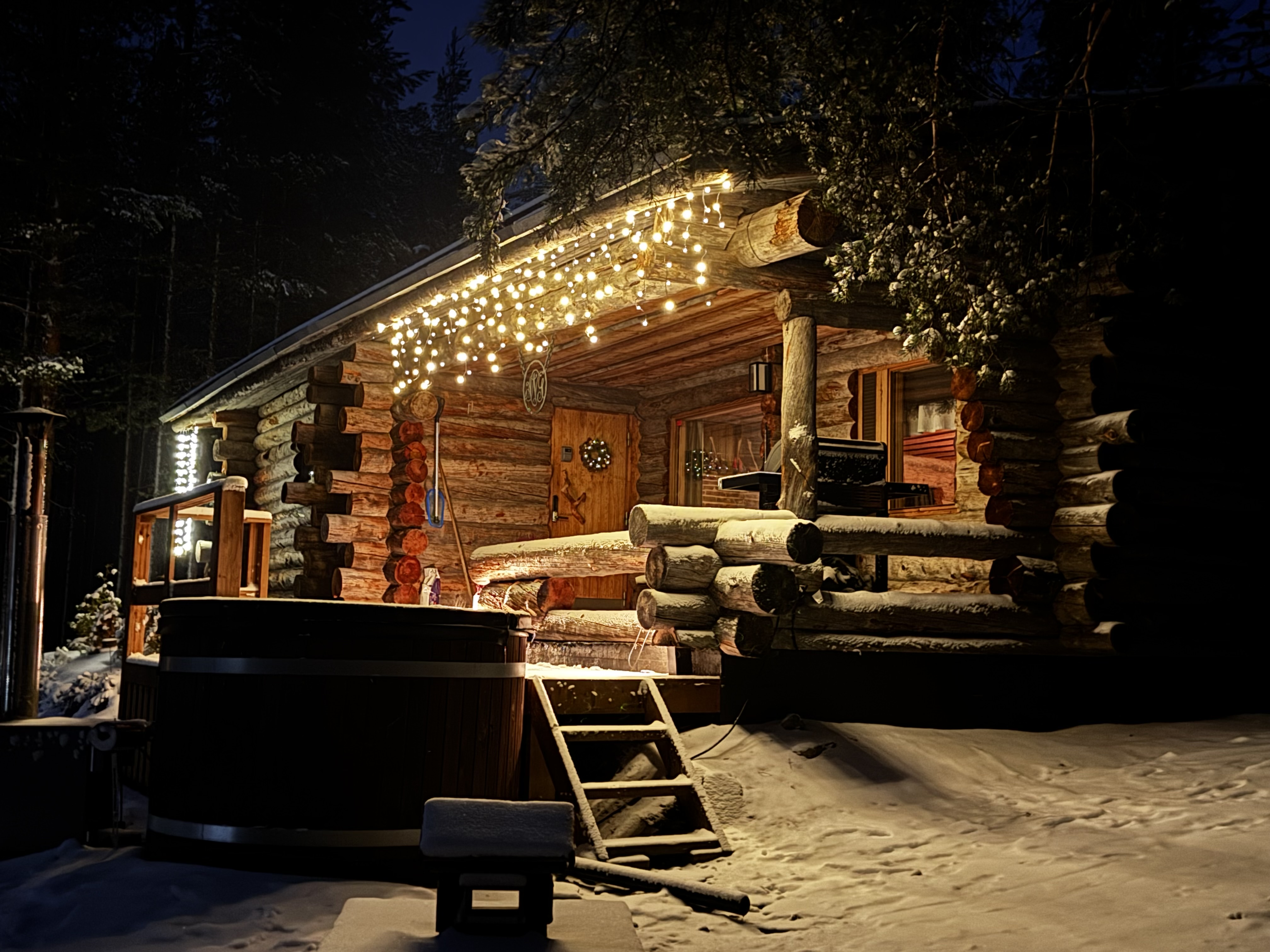 Valaistu kelohonkamökki lumisessa metsämaisemassa